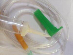 Clear medical IV set with tubing, green roller clamp, white spike, and brown injector, used for controlled fluid administration.