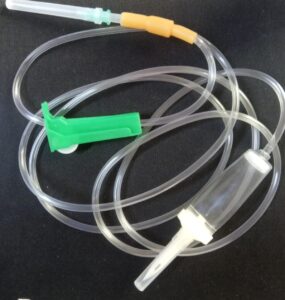 Clear medical IV set with tubing, green roller clamp, white spike, and brown injector, used for controlled fluid administration.