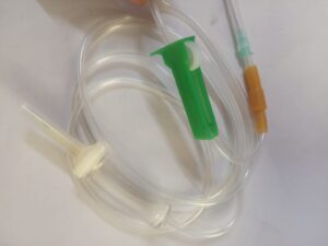 Clear medical IV set with tubing, green roller clamp, white spike, and brown injector, used for controlled fluid administration.